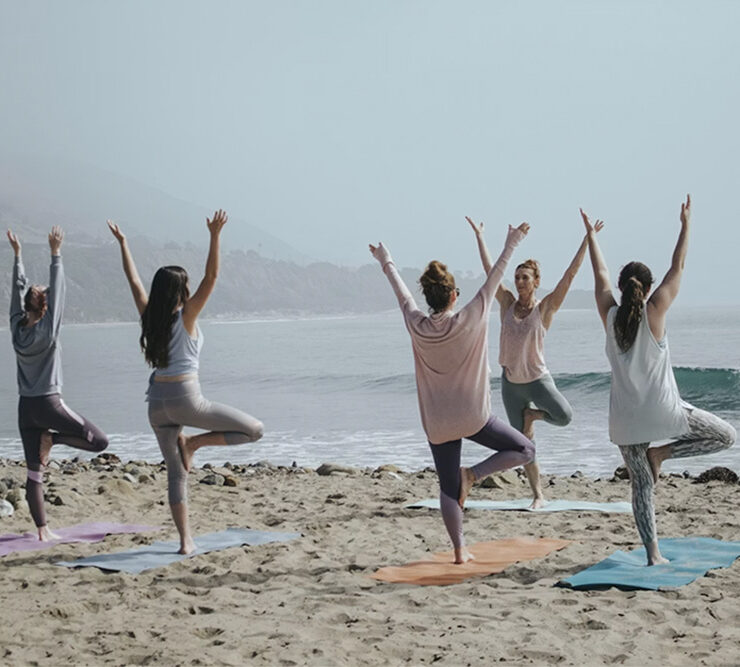 Yoga instructor leading a group of 4 woman exercising on the beach